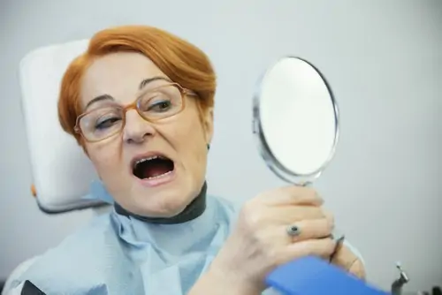 lady examines teeth in mirror in dental chair